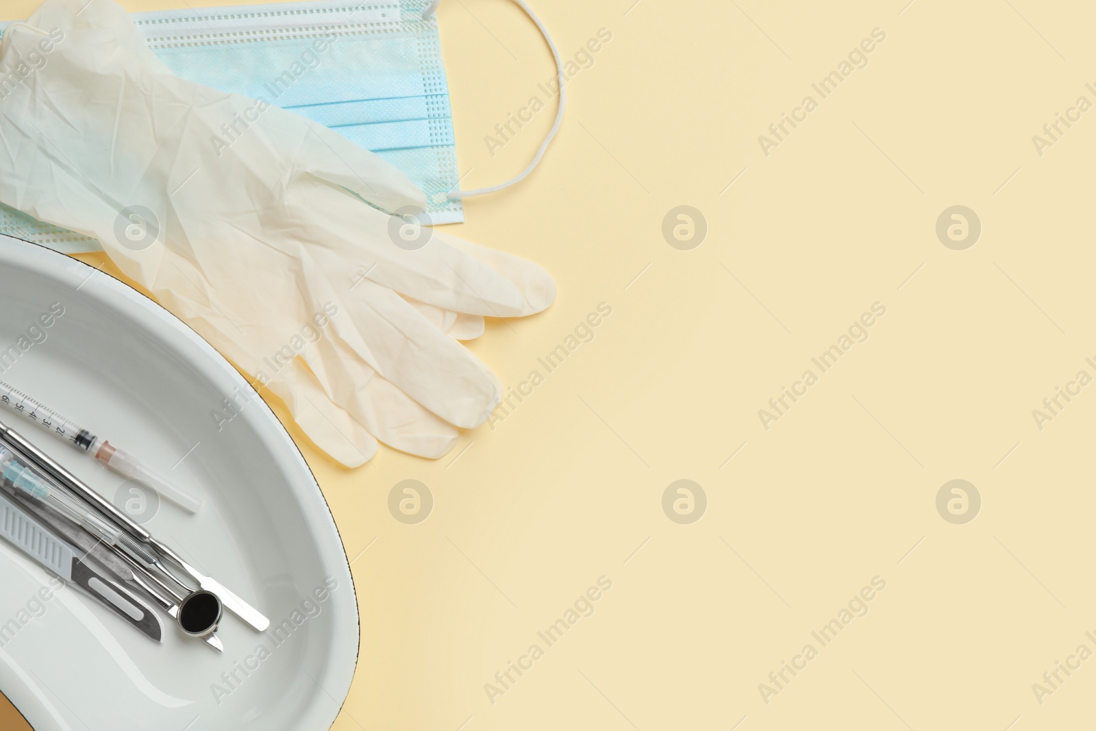 Photo of Set of different dentist's tools, face mask and glove on pale yellow background, flat lay. Space for text