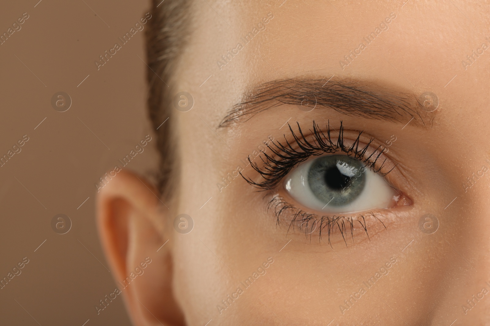 Photo of Woman with long eyelashes after mascara applying against light brown background, closeup