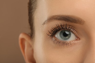Photo of Woman with long eyelashes after mascara applying against light brown background, closeup