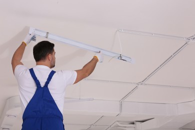 Photo of Ceiling light. Electrician installing led linear lamp indoors, back view. Space for text