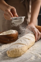 Photo of Woman pouring flour onto loaf of raw bread at table, closeup