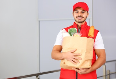 Photo of Food delivery courier holding paper bag with products indoors. Space for text