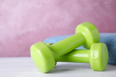 Stylish dumbbells and towel on table against color background, space for text. Home fitness