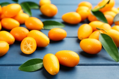 Fresh ripe kumquats and leaves on blue wooden table, closeup