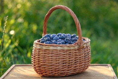 Wicker basket of tasty ripe blueberries on wooden surface outdoors, closeup. Seasonal berries