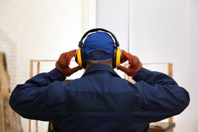 Photo of Worker wearing safety headphones indoors, back view. Hearing protection device