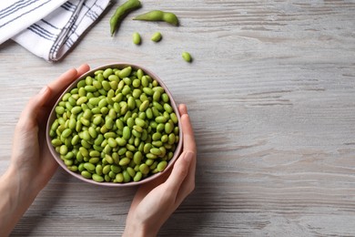 Photo of Woman holding bowl of edamame beans at light wooden table, closeup. Space for text