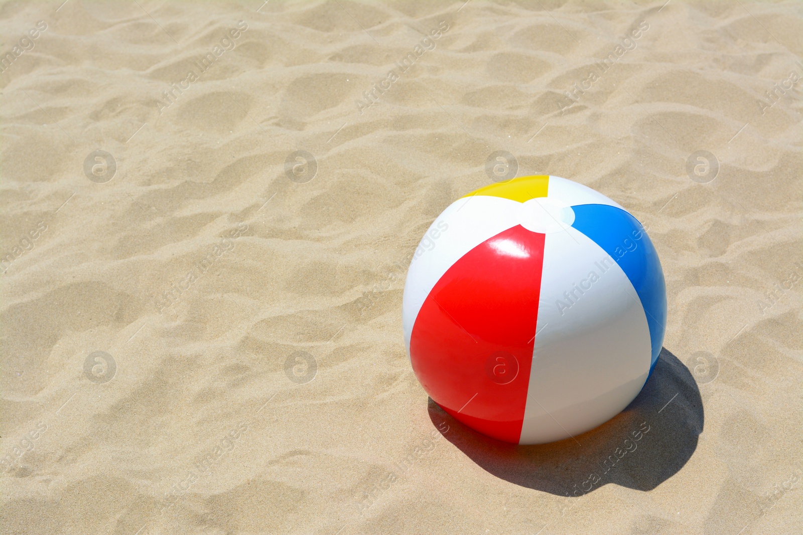 Photo of Colorful beach ball on sand, space for text