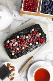 Delicious chocolate sponge cake, tea and ingredients on white marble table, flat lay