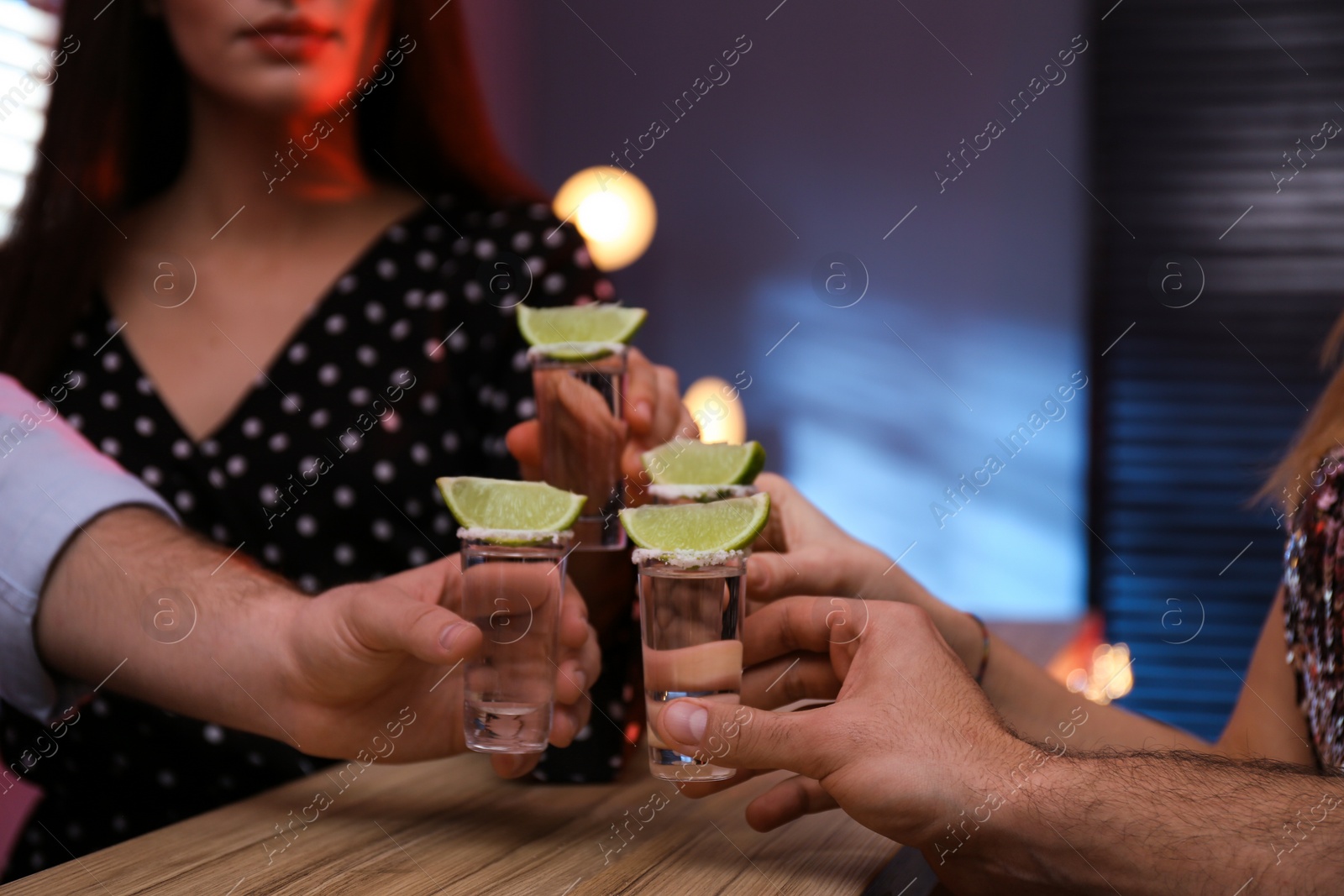 Photo of Young people toasting with Mexican Tequila shots at bar, closeup