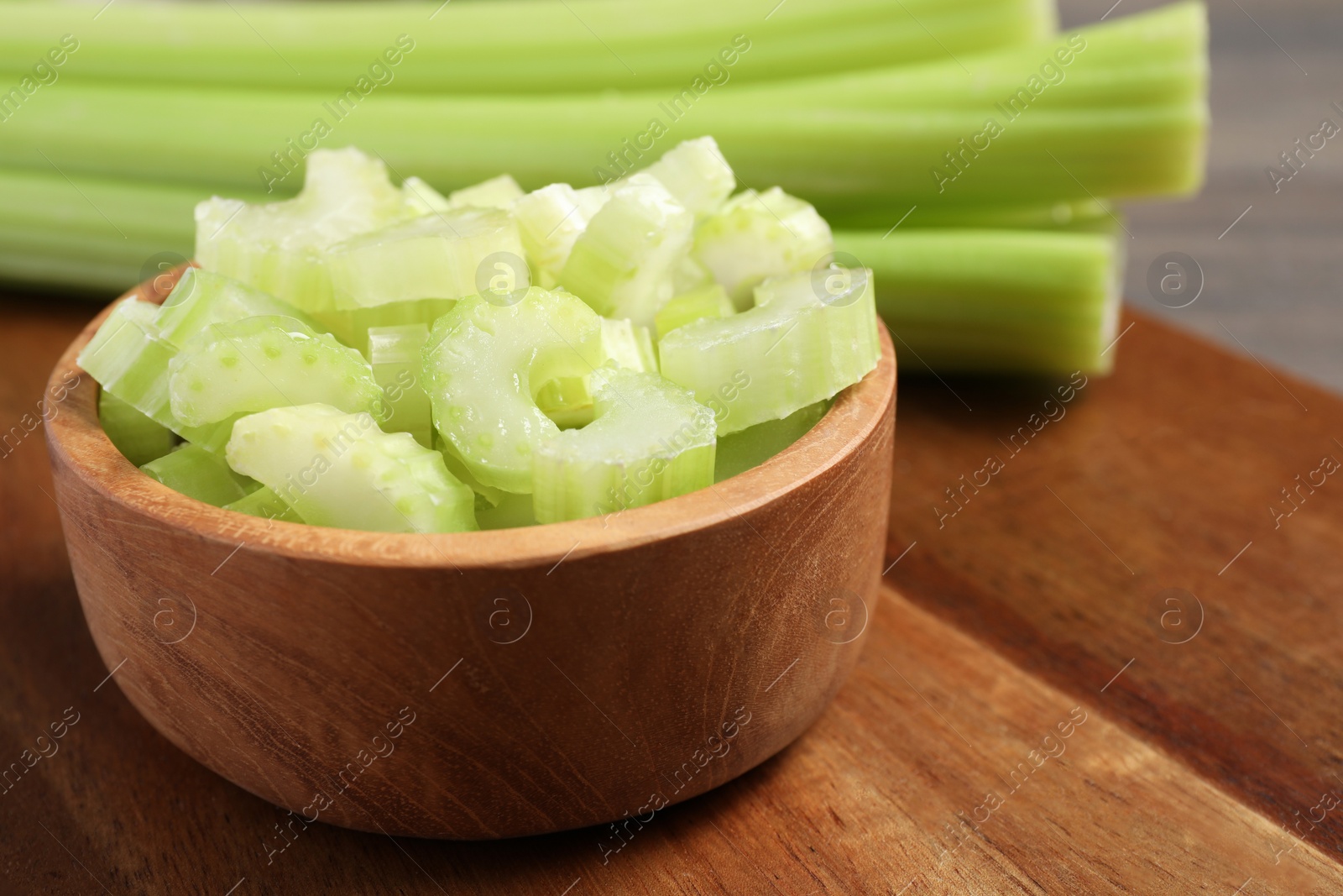 Photo of Bowl with fresh green cut celery on wooden board, closeup. Space for text