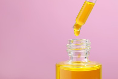Photo of Dripping yellow serum from pipette into bottle on pink background, closeup. Space for text