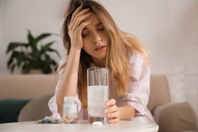 Woman taking medicine for hangover at home, focus on hand