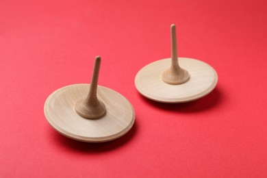 Photo of Two wooden spinning tops on red background, closeup