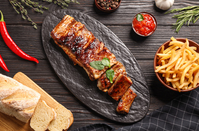 Delicious grilled ribs served on black wooden table, flat lay