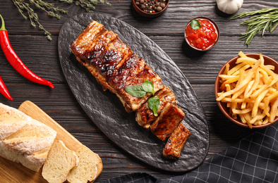 Photo of Delicious grilled ribs served on black wooden table, flat lay