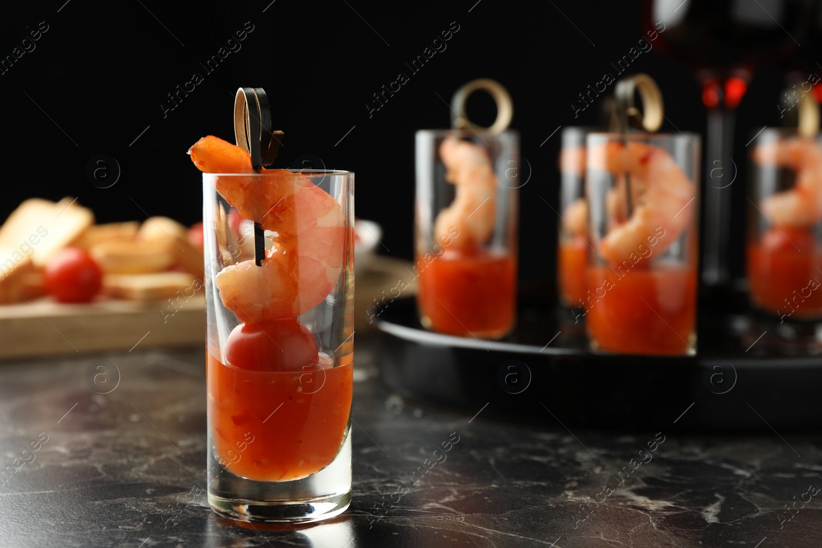 Photo of Tasty canape with shrimp, tomato and sauce in shot glass on black marble table, closeup. Space for text