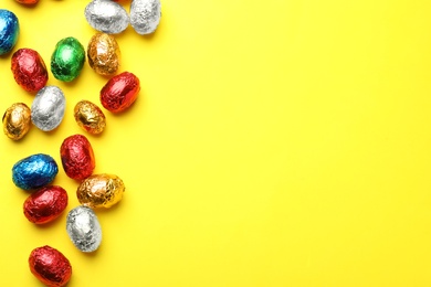 Photo of Chocolate eggs wrapped in colorful foil on yellow background, flat lay. Space for text