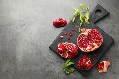 Photo of Cut fresh pomegranate and green leaves on grey table, top view. Space for text