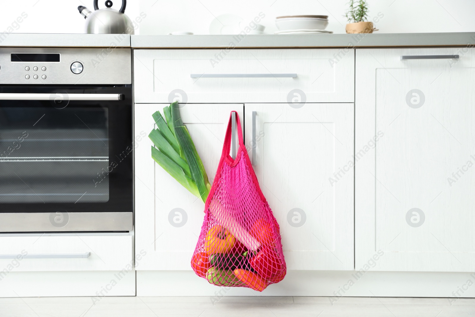 Photo of Net bag with vegetables hanging on cabinet door in kitchen