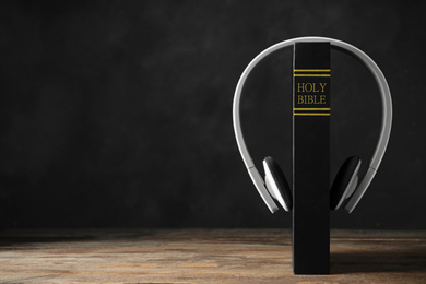 Bible and headphones on wooden table, space for text. Religious audiobook