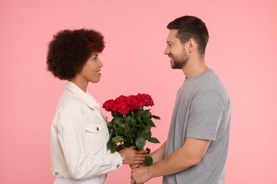 Photo of International dating. Lovely couple with bouquet of roses on pink background
