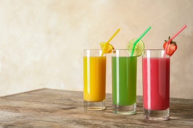 Three glasses of different juices with straws on table. Space for text