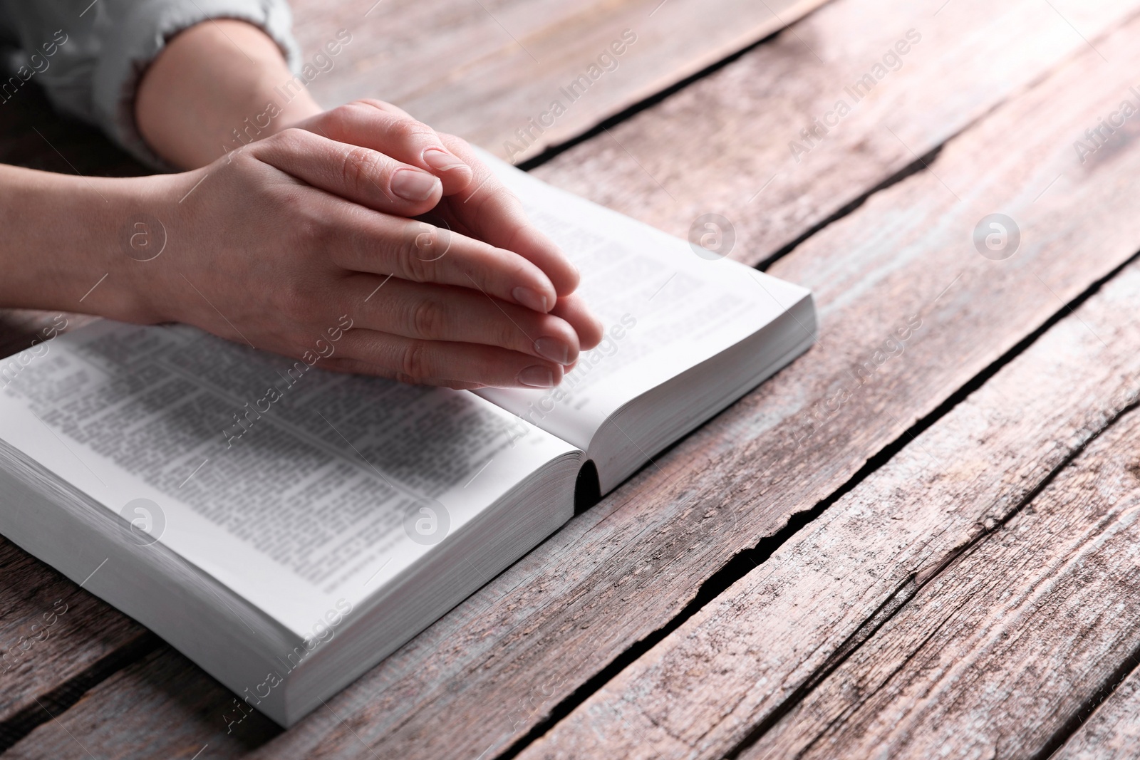 Photo of Religion. Christian woman praying over Bible at wooden table, closeup