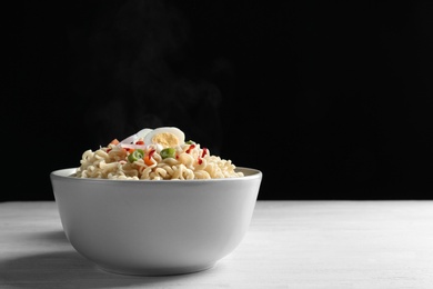 Photo of Bowl of hot noodles with egg and vegetables on table against black background. Space for text