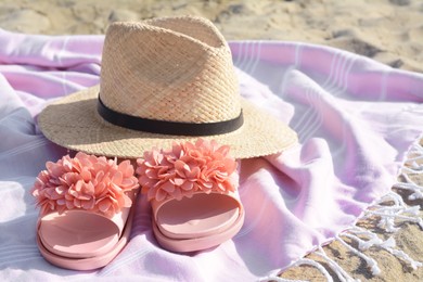 Blanket with stylish slippers and straw hat on sandy beach, closeup