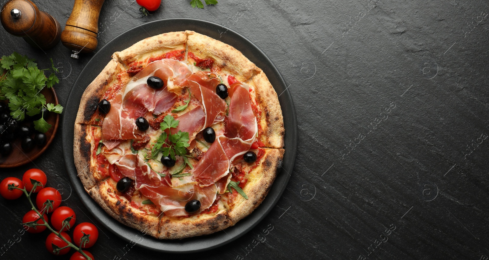 Photo of Tasty pizza with cured ham, olives, tomatoes and parsley on black table, top view. Space for text