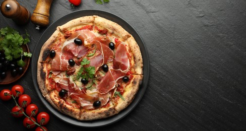 Photo of Tasty pizza with cured ham, olives, tomatoes and parsley on black table, top view. Space for text