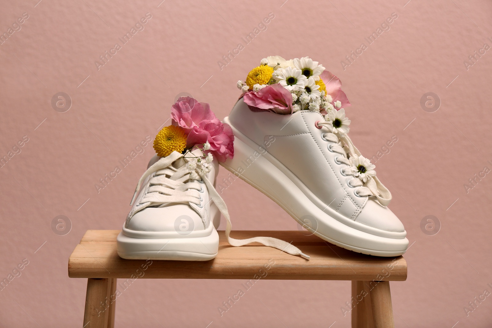 Photo of Shoes with beautiful flowers on wooden stand against pale pink background