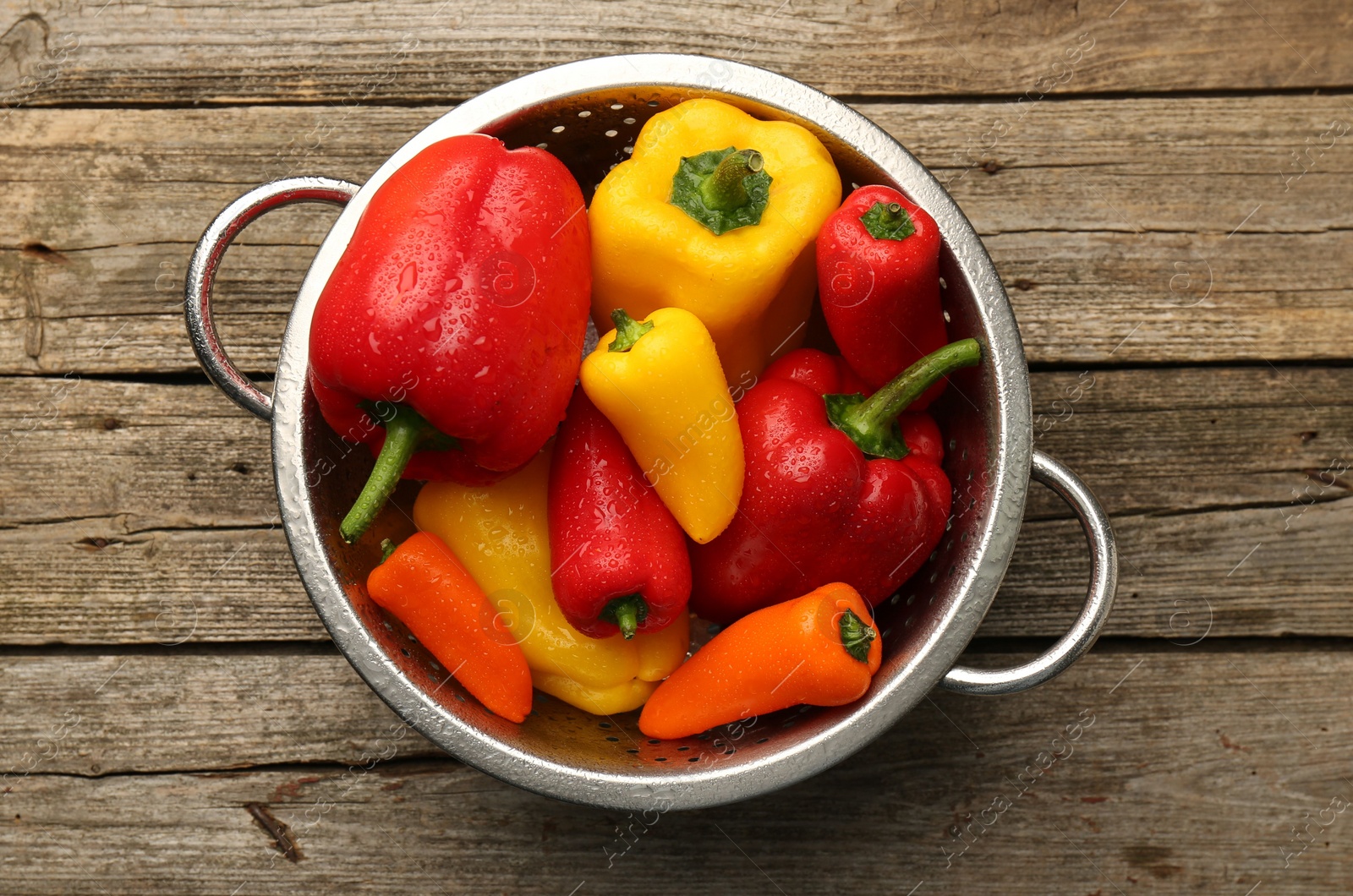 Photo of Metal colander with fresh peppers on wooden table, top view