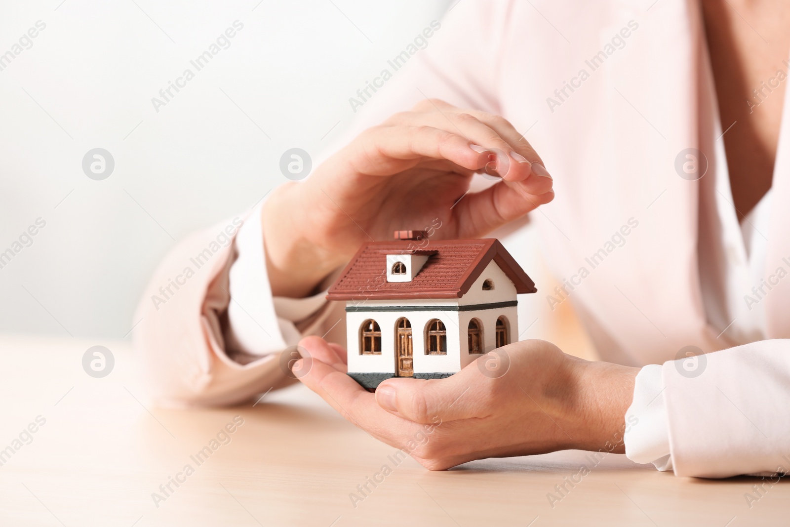 Photo of Female agent covering house model at table, closeup. Home insurance