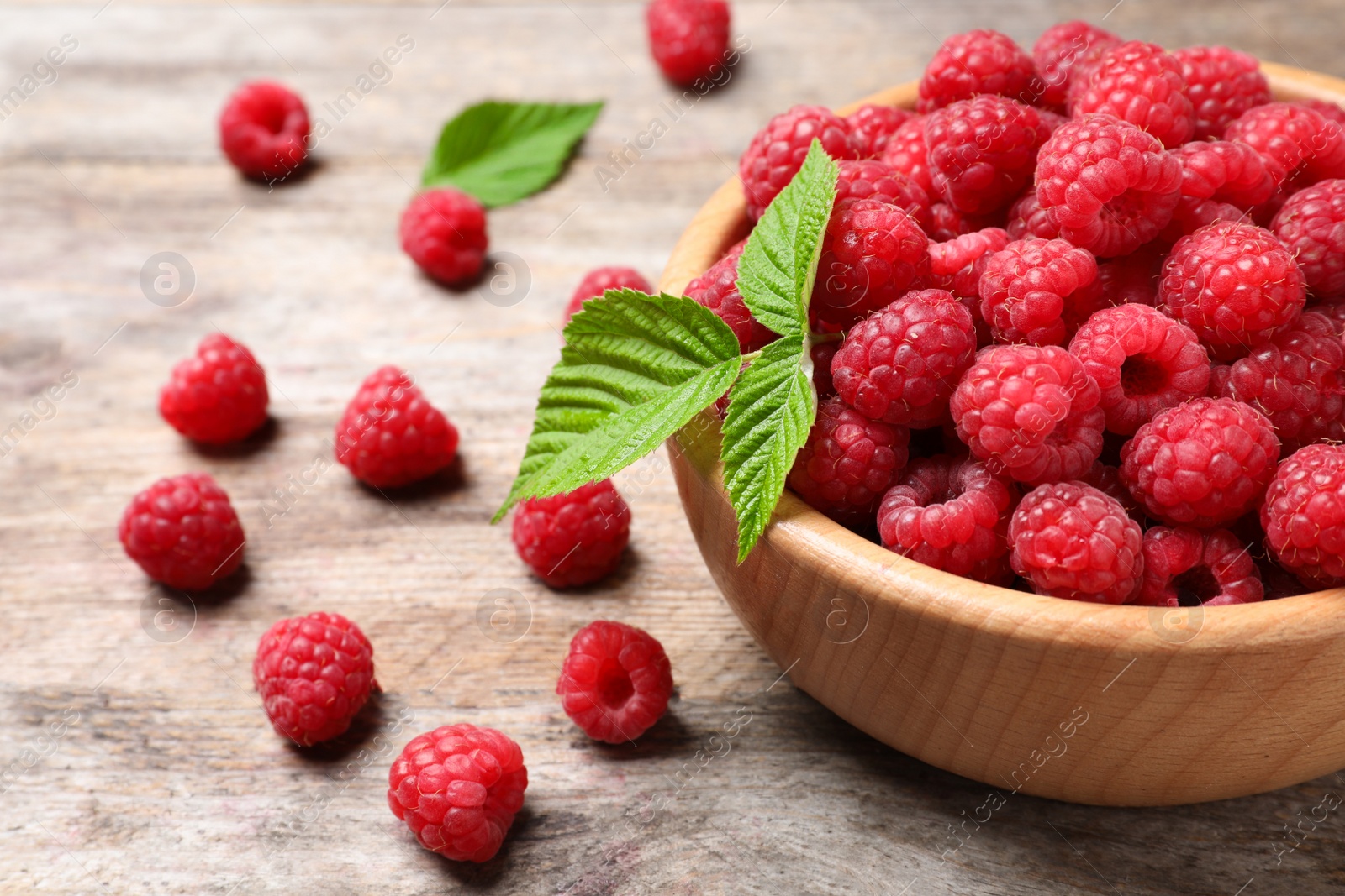 Photo of Bowl with ripe aromatic raspberries on wooden table