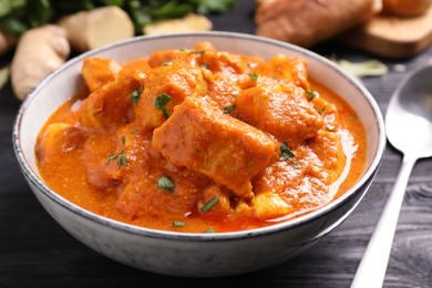 Photo of Bowl of delicious chicken curry on black wooden table, closeup