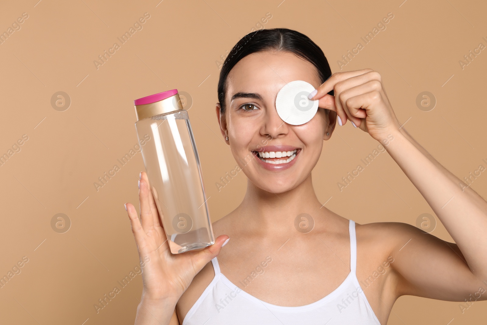 Photo of Young woman using cotton pad with micellar water on beige background