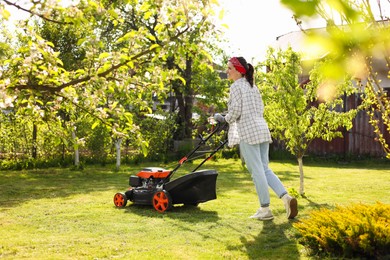Woman cutting green grass with lawn mower in garden