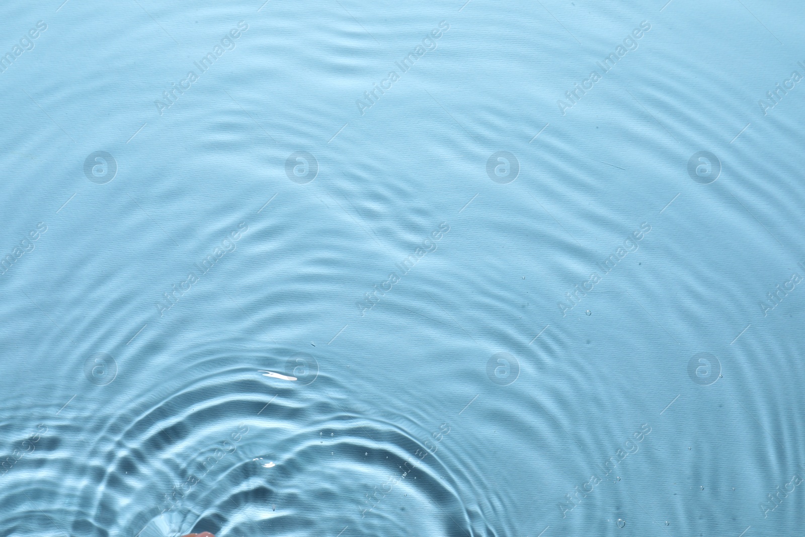 Photo of Rippled surface of clear water on light blue background, top view