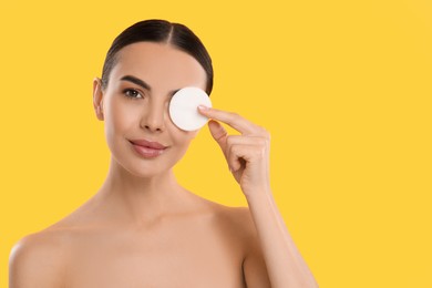 Photo of Beautiful woman removing makeup with cotton pad on yellow background, space for text