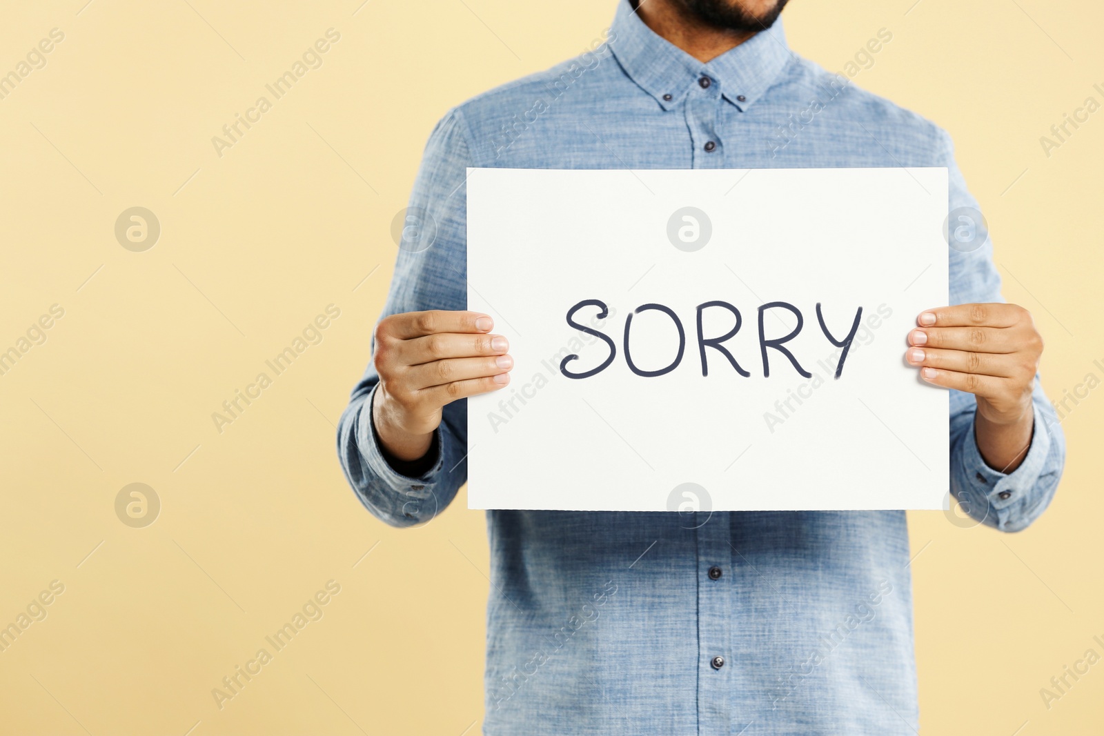 Image of Apology. Man holding card with word Sorry on beige background, closeup