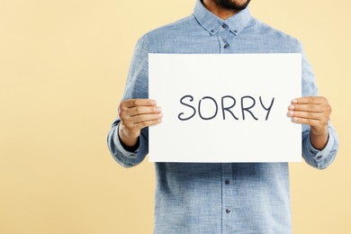 Image of Apology. Man holding card with word Sorry on beige background, closeup