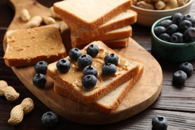 Photo of Delicious toasts with peanut butter, blueberries and nuts on wooden table, closeup