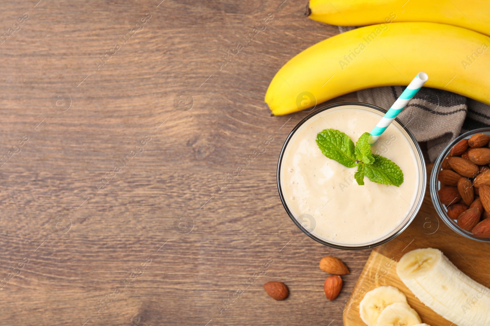 Photo of Flat lay composition of banana smoothie in glass and nuts on wooden table. Space for text