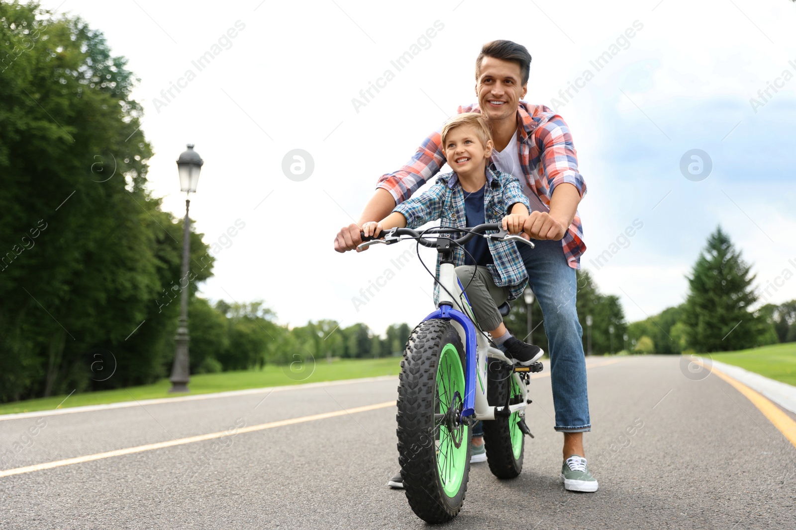 Image of Dad teaching son to ride bicycle outdoors