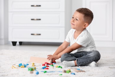 Motor skills development. Little boy playing with colorful wooden pieces on floor indoors