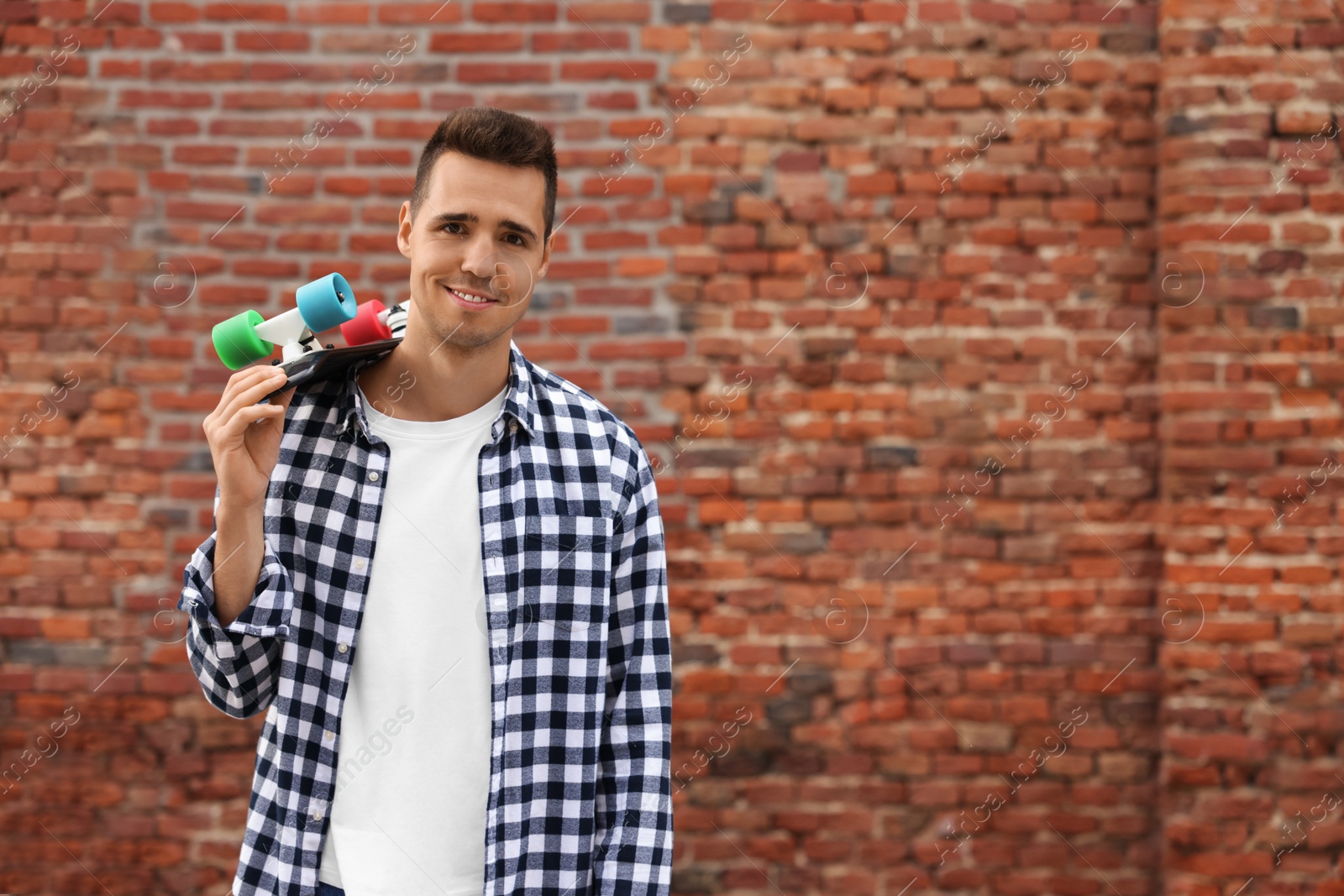 Photo of Portrait of young man with skateboard near brick wall outdoors, space for text. Hip hop dancer