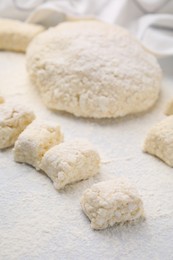 Photo of Making lazy dumplings. Raw dough and flour on white tiled table, closeup