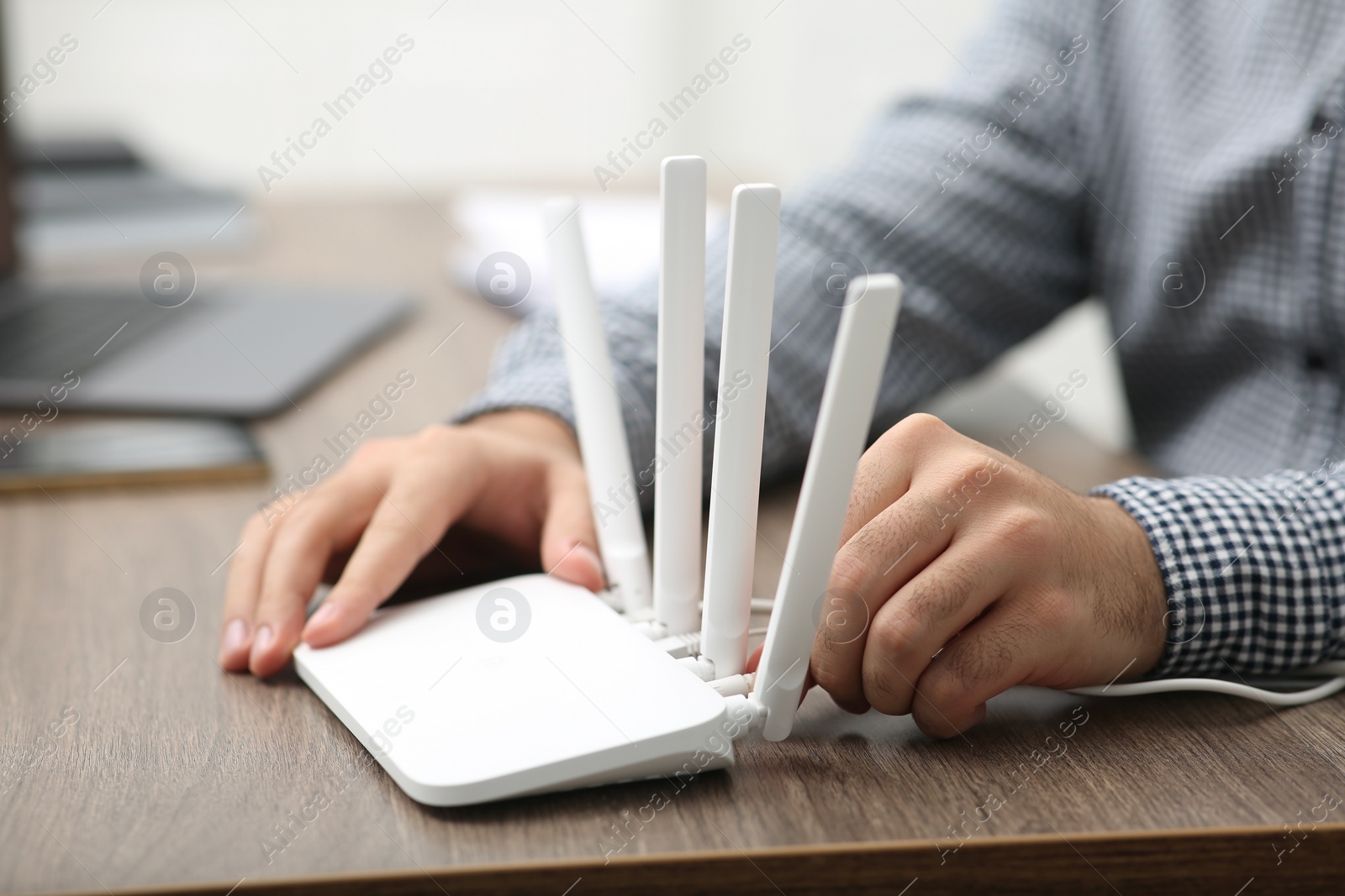 Photo of Man inserting cable into Wi-Fi router at wooden table indoors, closeup